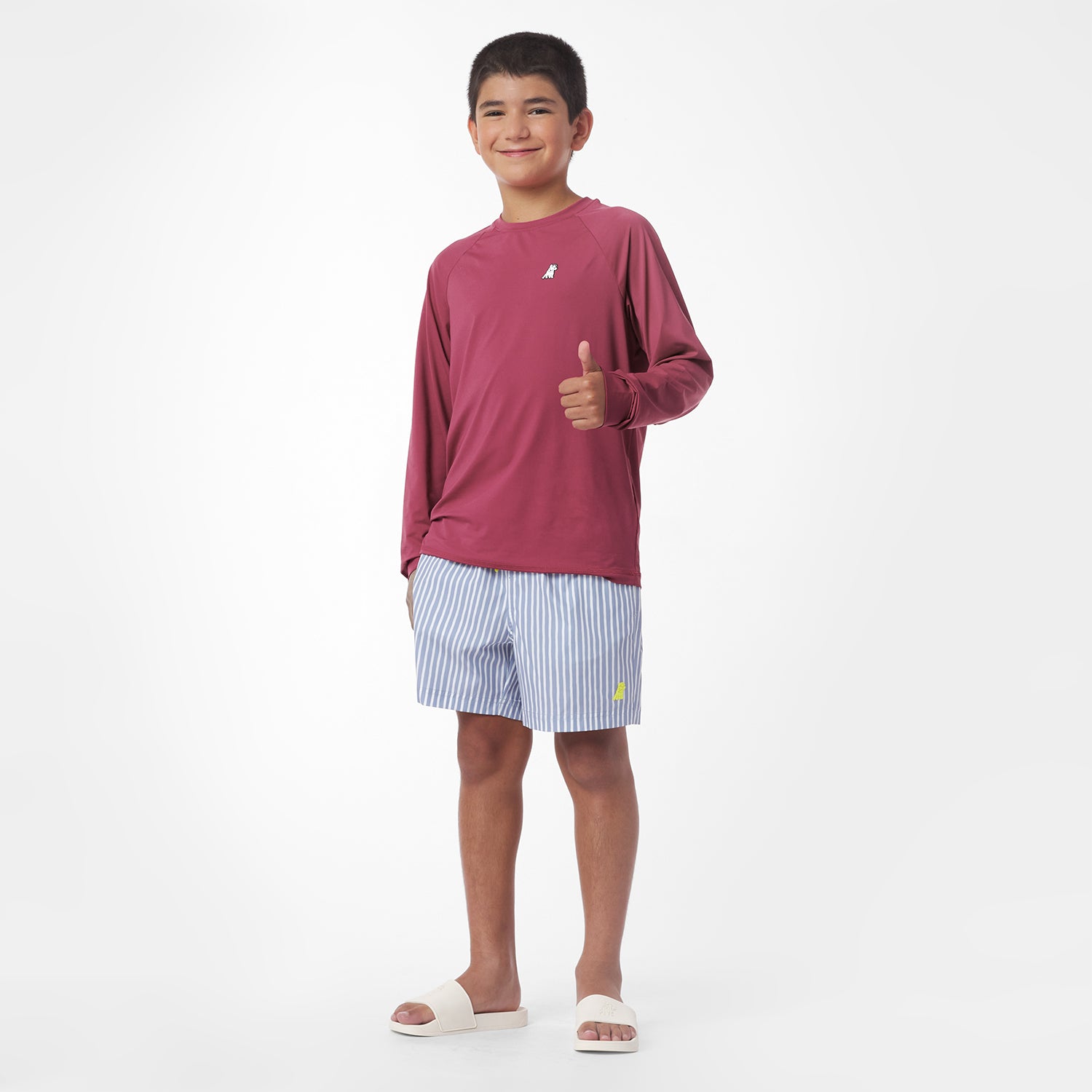 Child wearing a maroon long-sleeve rashguard and striped shorts on a white background