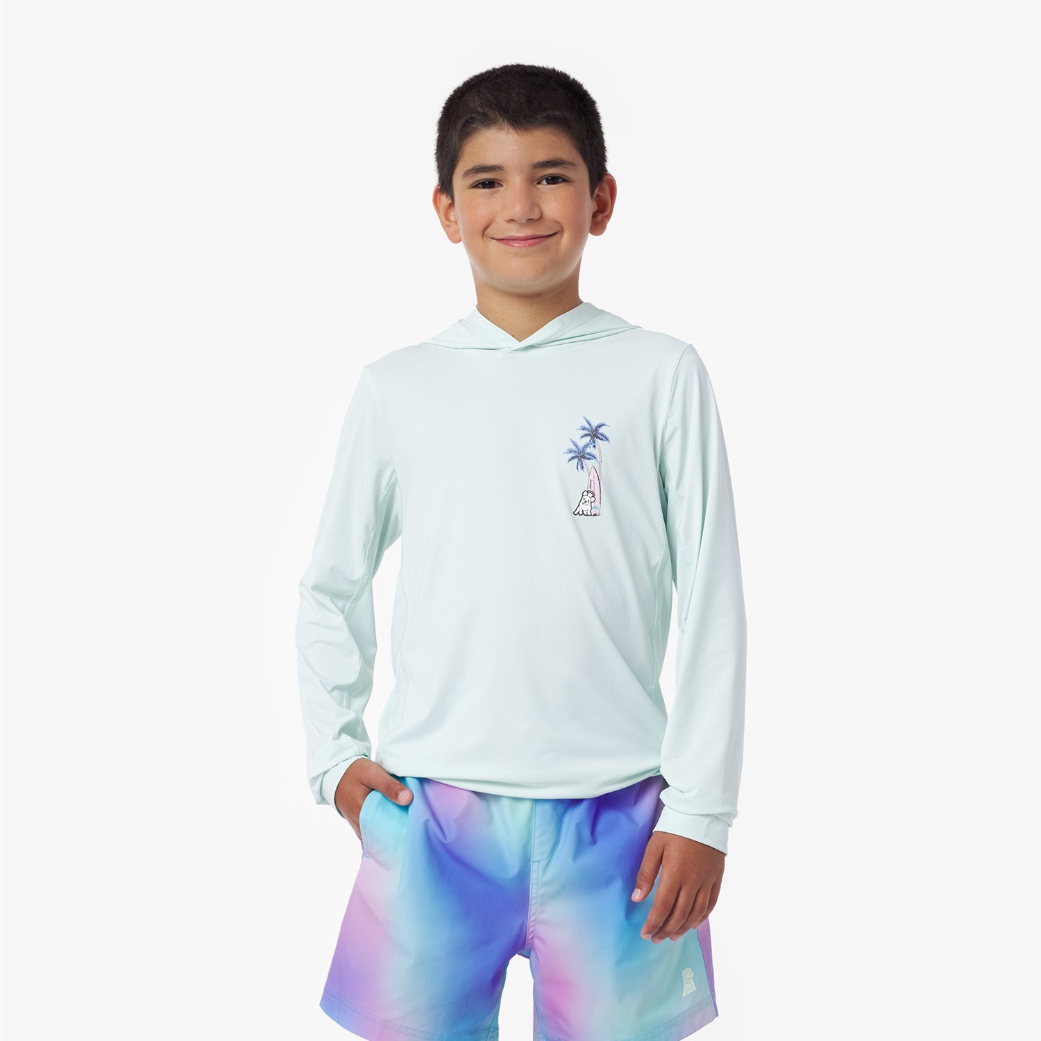 Boy wearing a light blue rashguard with a palm tree design and colorful shorts