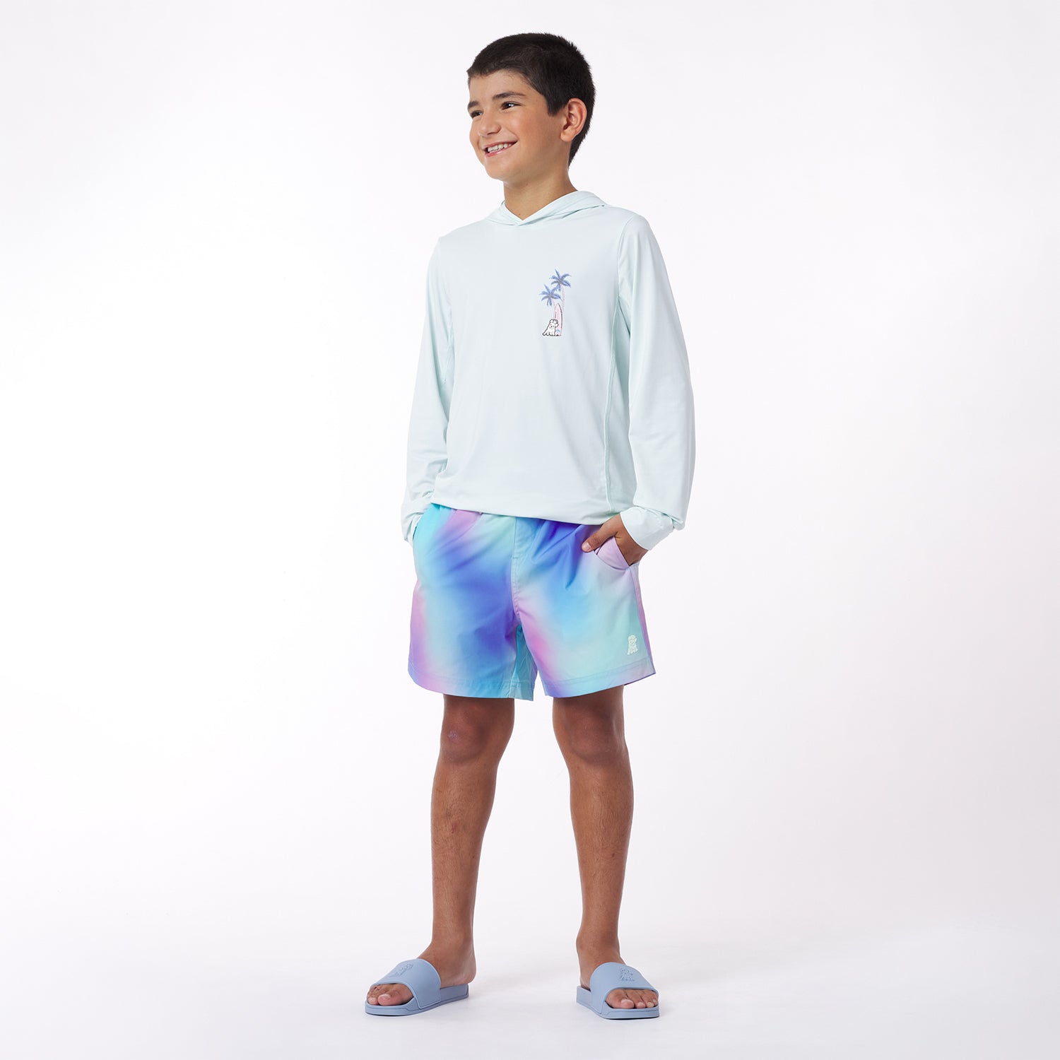Child wearing a light blue rashguard and tie-dye shorts on a white background