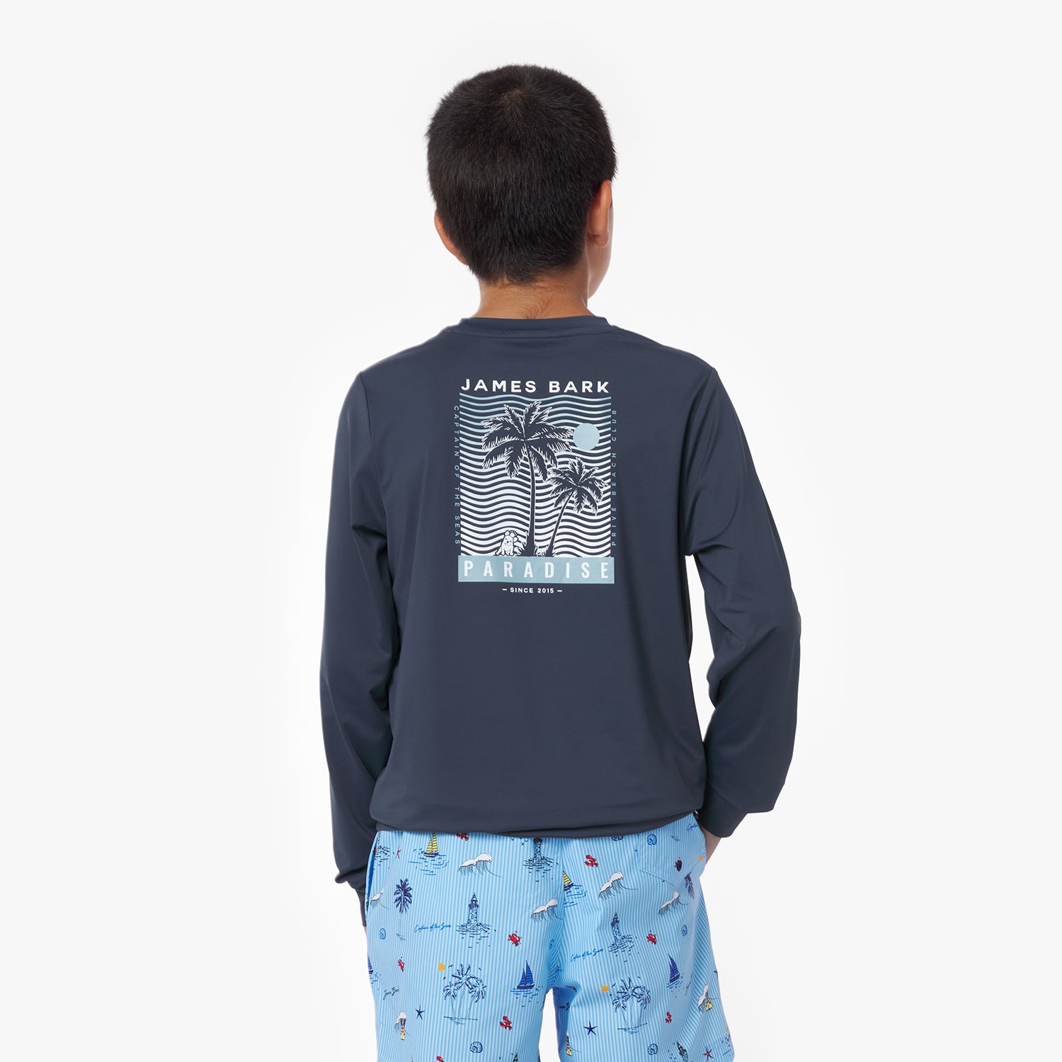 Boy wearing a navy rashguard with a palm tree design and 'James Bark' text on the back