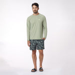 Man wearing a green long-sleeve rashguard and patterned shorts on a white background