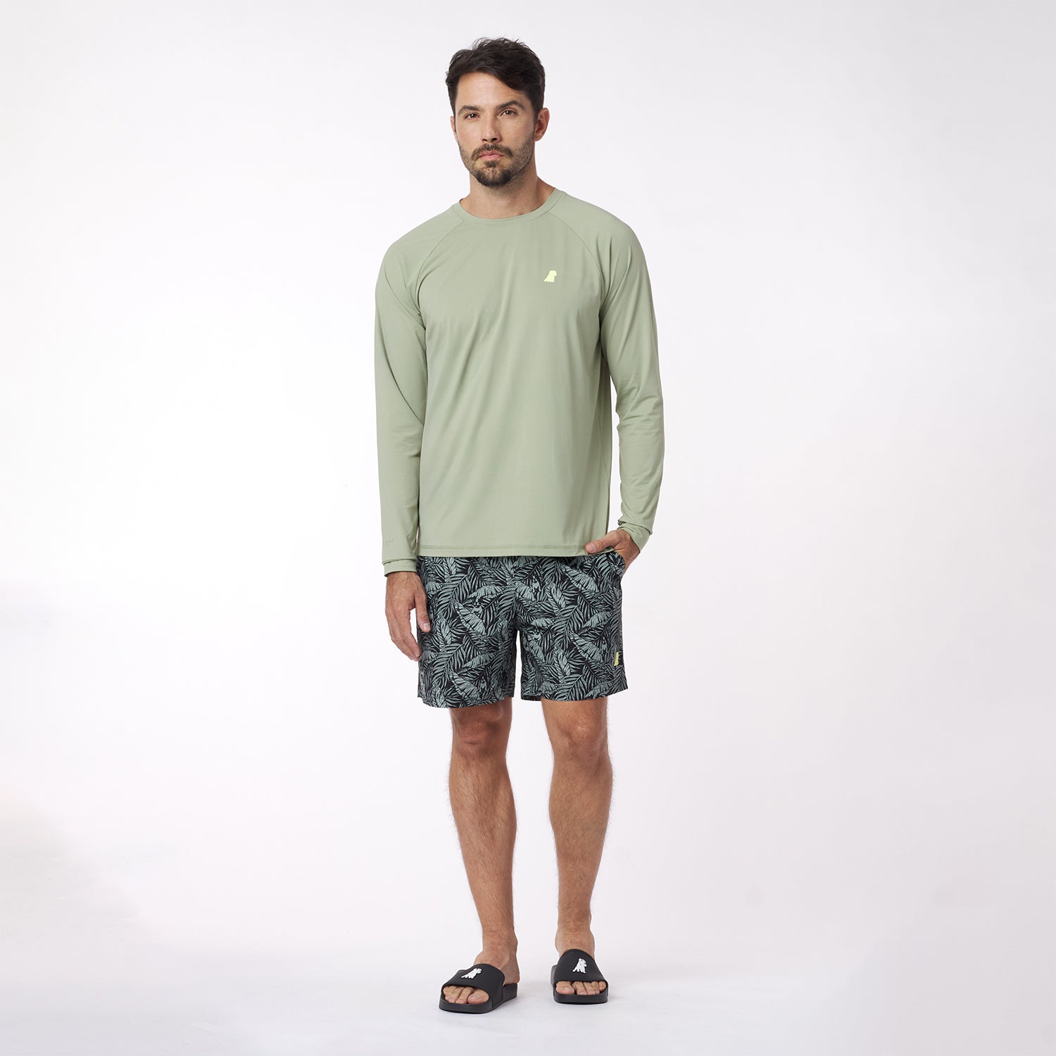 Man wearing a green long-sleeve rashguard and patterned shorts on a white background