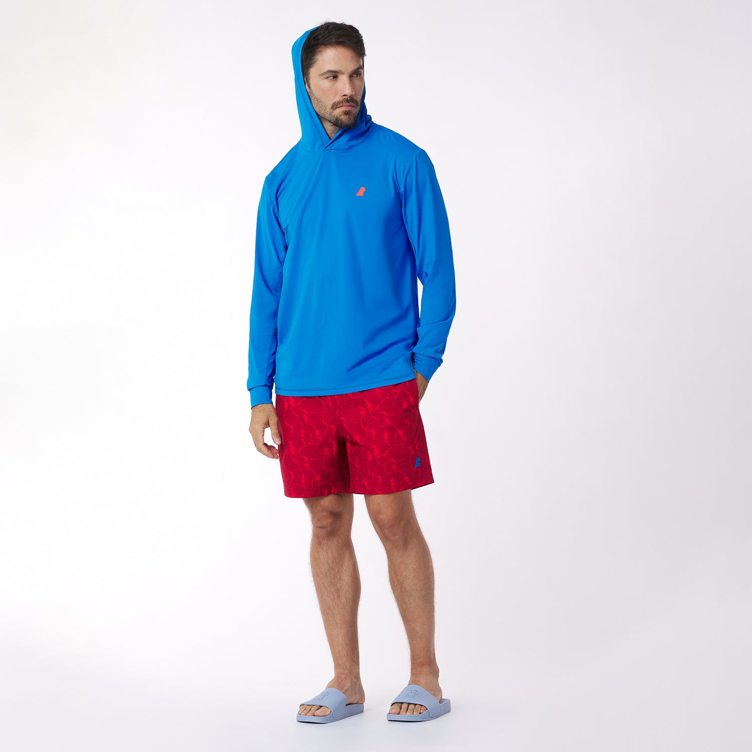 Man wearing a blue hooded rashguard and red swim shorts on a white background