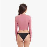 Back view of a woman wearing a pink long-sleeve rashguard and black bikini bottom