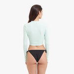 Back view of a woman wearing a light green long-sleeve rashguard and black bikini bottom