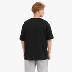 Back view of a man wearing a black t-shirt and gray shorts on a white background