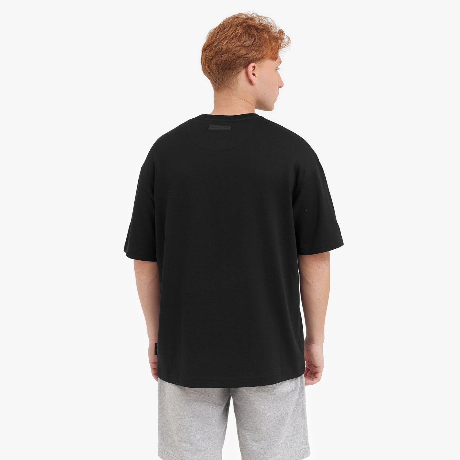 Back view of a man wearing a black t-shirt and gray shorts on a white background