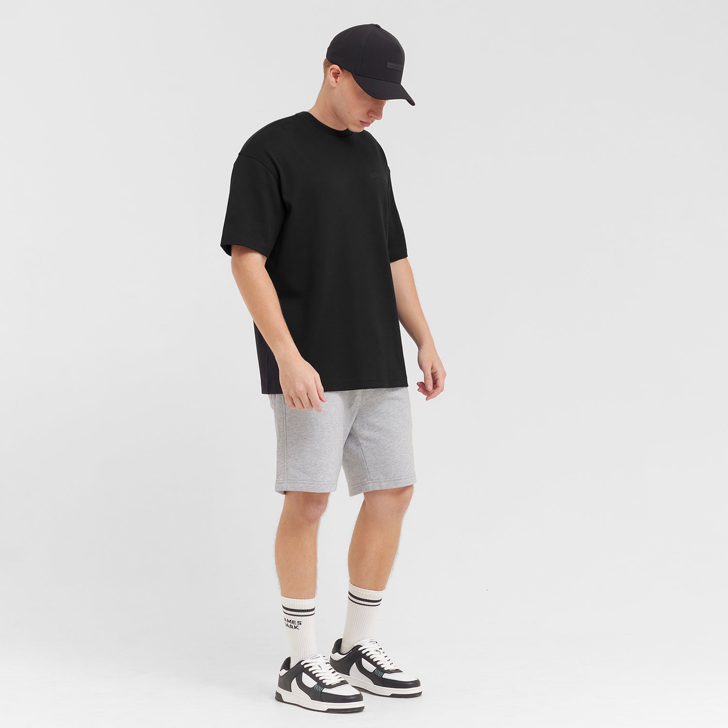 Man wearing a black t-shirt, gray shorts, and black and white sneakers on a white background