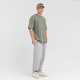 Person wearing a green t-shirt, gray sweatpants, and a green cap on a white background