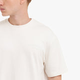 Close-up of a person wearing a plain white t-shirt on a light beige background