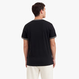 Back view of a man wearing a black t-shirt with white trim on a white background