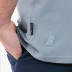 Close-up of a light blue shirt with a logo on the chest pocket against a white background