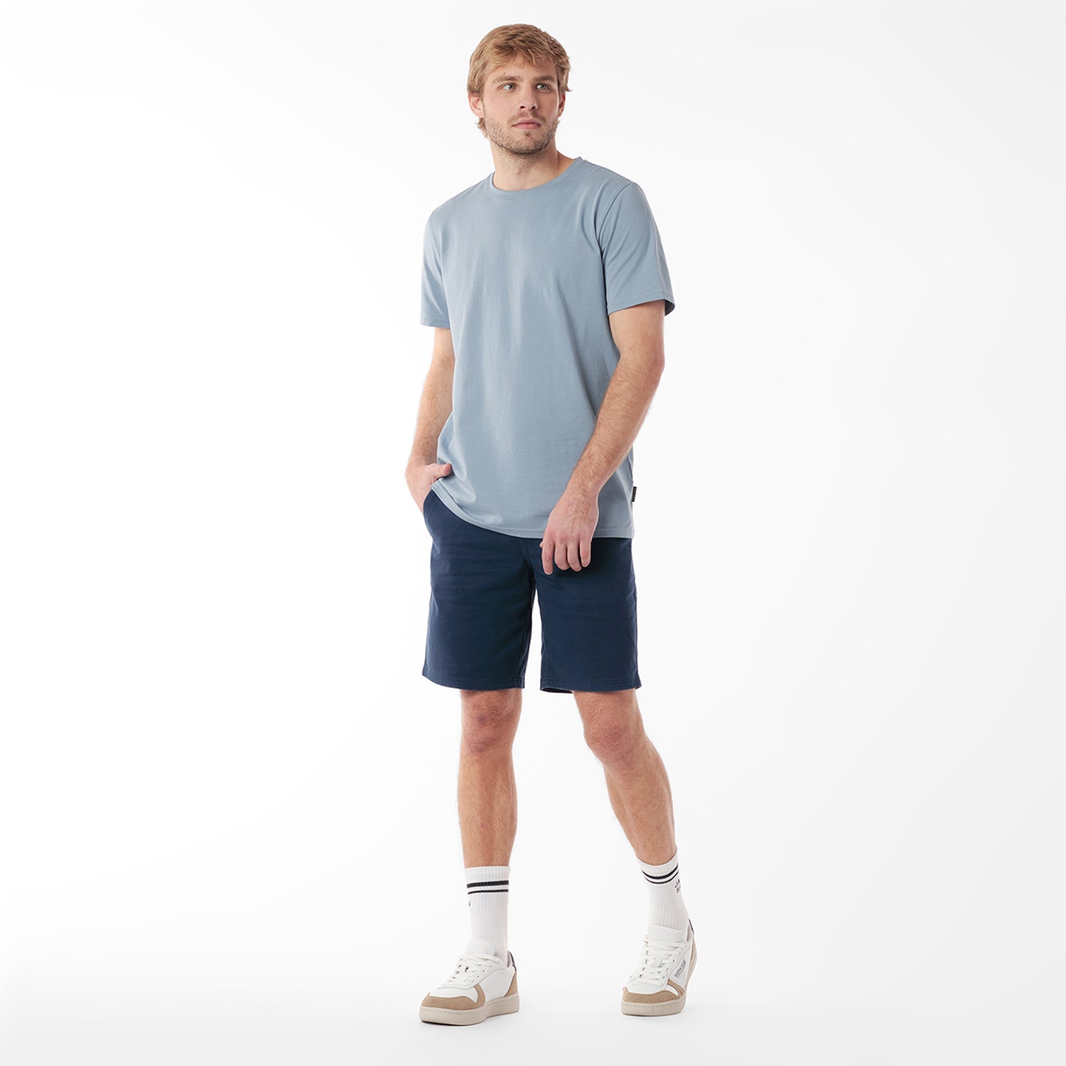 Full body picture of man wearing a light blue t-shirt and navy shorts on a white background