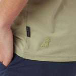 Close-up of a green shirt with a brand logo and label on a person wearing navy pants.
