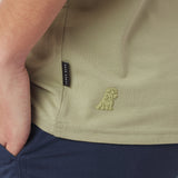 Close-up of a green shirt with a brand logo and label on a person wearing navy pants.