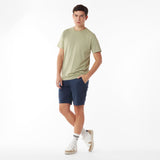 Full body picture of a man wearing a light green t-shirt and navy shorts on a white background