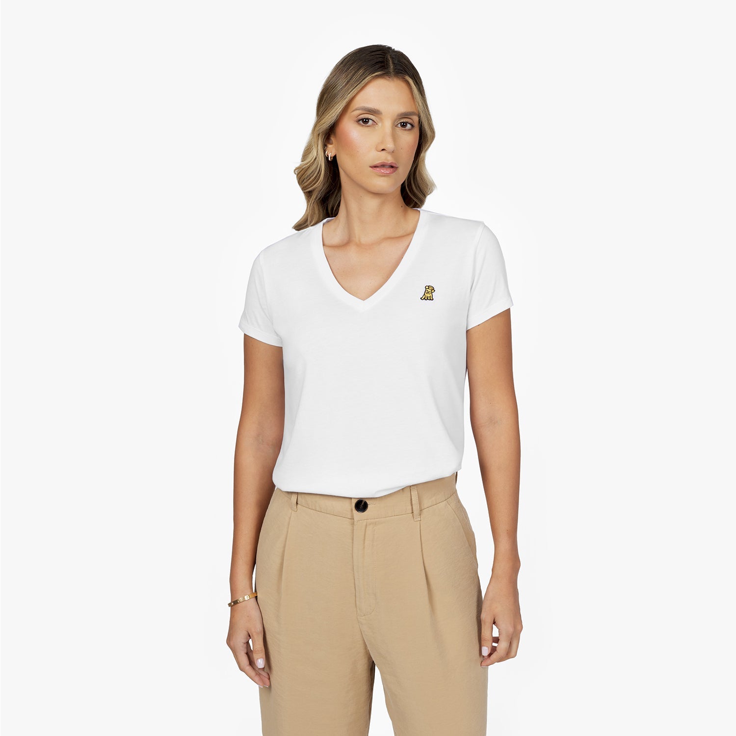Front waist-up view of a female model wearing a white v-neck t-shirt with a small gold embroidered logo on the left chest, paired with beige trousers