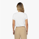 Back waist-up view of a female model wearing a plain white short-sleeve t-shirt tucked into beige trousers