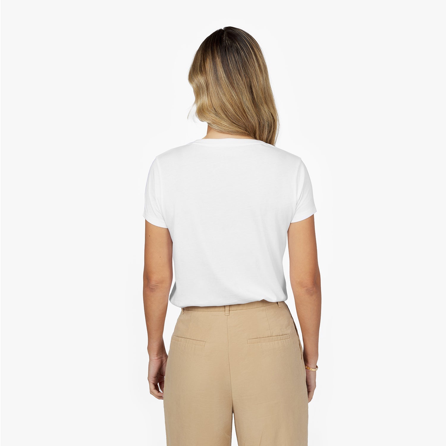 Back waist-up view of a female model wearing a plain white short-sleeve t-shirt tucked into beige trousers