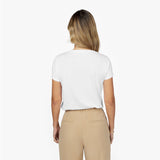 Back waist-up view of a female model wearing a plain white short-sleeve t-shirt tucked into beige trousers