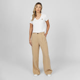 Full-length front view of a female model wearing a white v-neck t-shirt with a gold logo, wide-leg beige trousers, and white sneakers, standing against a light grey background