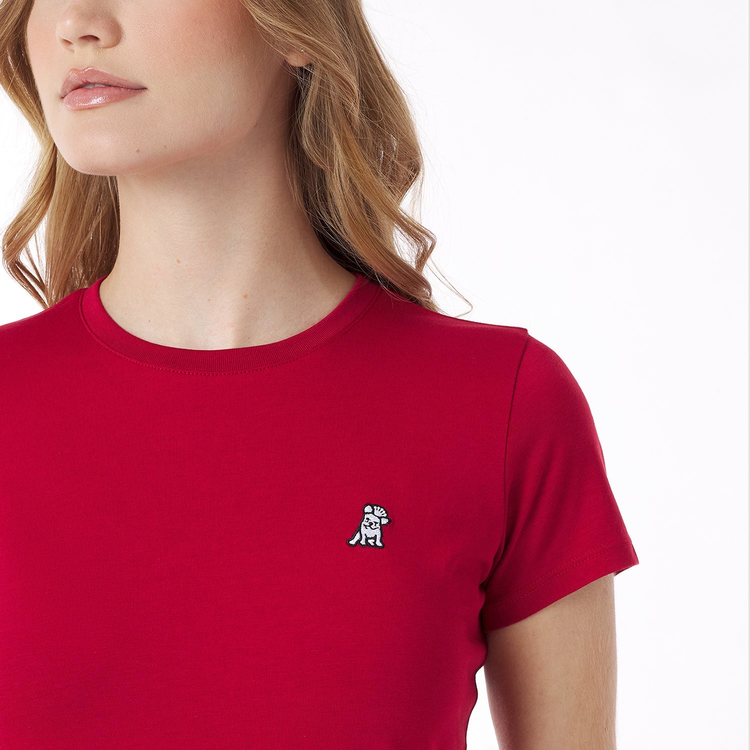 Close-up of a red t-shirt with a small logo worn by a person on a white background