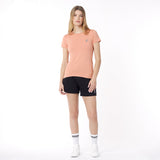 Full body view of a woman wearing a peach t-shirt and black shorts on a white background