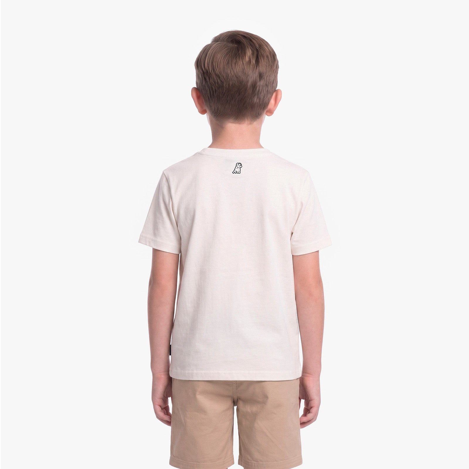 A child viewed from the back wearing a light cream/off-white short-sleeve t-shirt with a small black graphic on the upper back