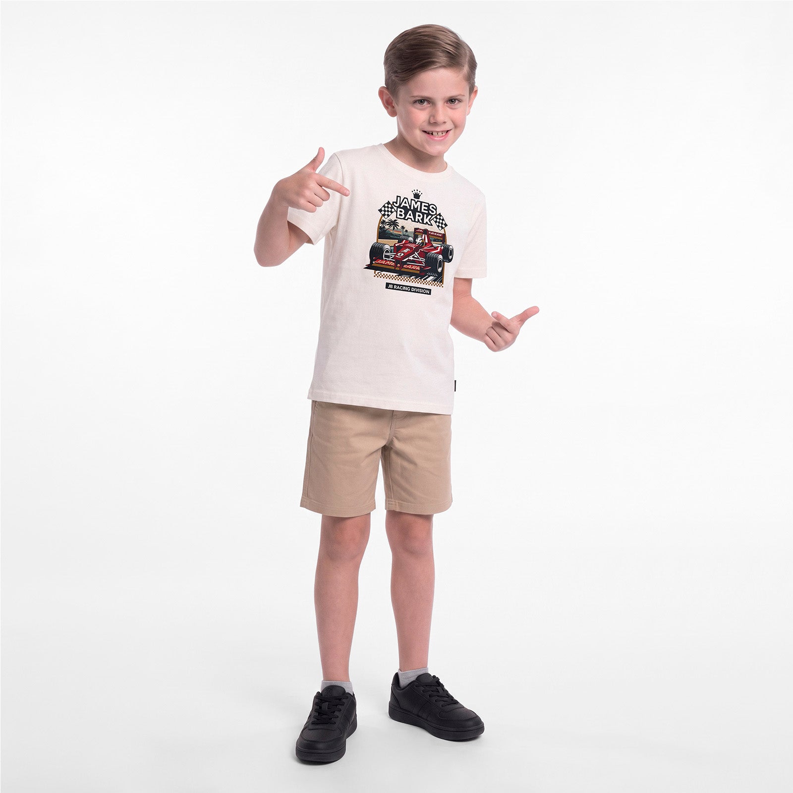 A young boy modeling a cream-colored graphic t-shirt, khaki shorts, and black sneakers against a plain white studio background.