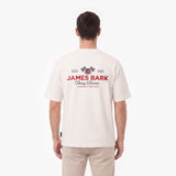 A man viewed from behind wearing a cream-colored short-sleeve t-shirt with a red and black James Bark Racing Division graphic on the back