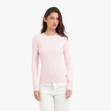 Woman wearing a light pink long-sleeve top and white pants on a white background