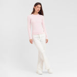 Woman wearing a light pink sweater and white pants on a plain background