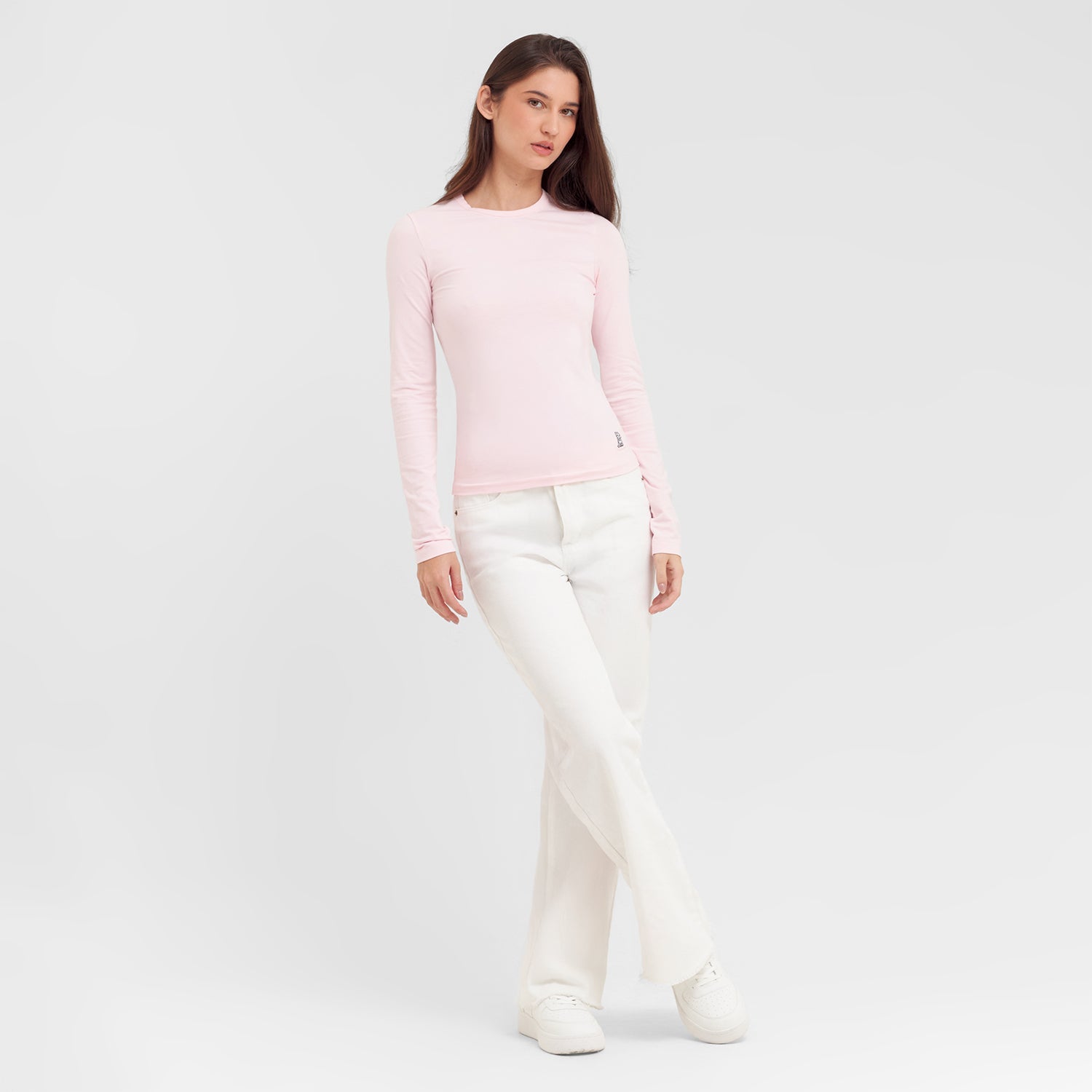 Woman wearing a light pink sweater and white pants on a plain background