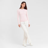 Woman wearing a light pink sweater and white pants on a plain background