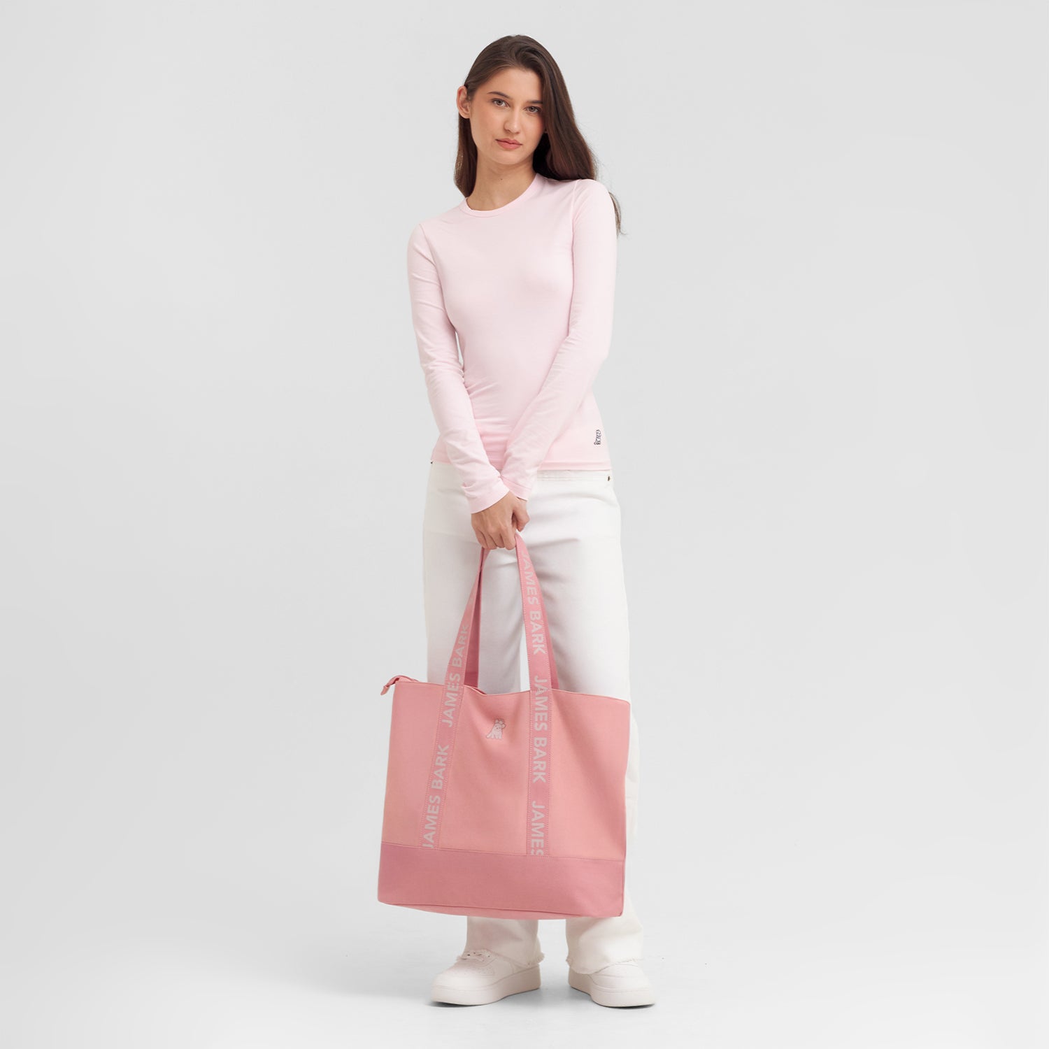 Woman holding a pink tote bag against a light gray background