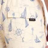 Close-up of a light cream short-sleeve button-up shirt with a blue nautical print of sailboats, compass roses, and palm trees.