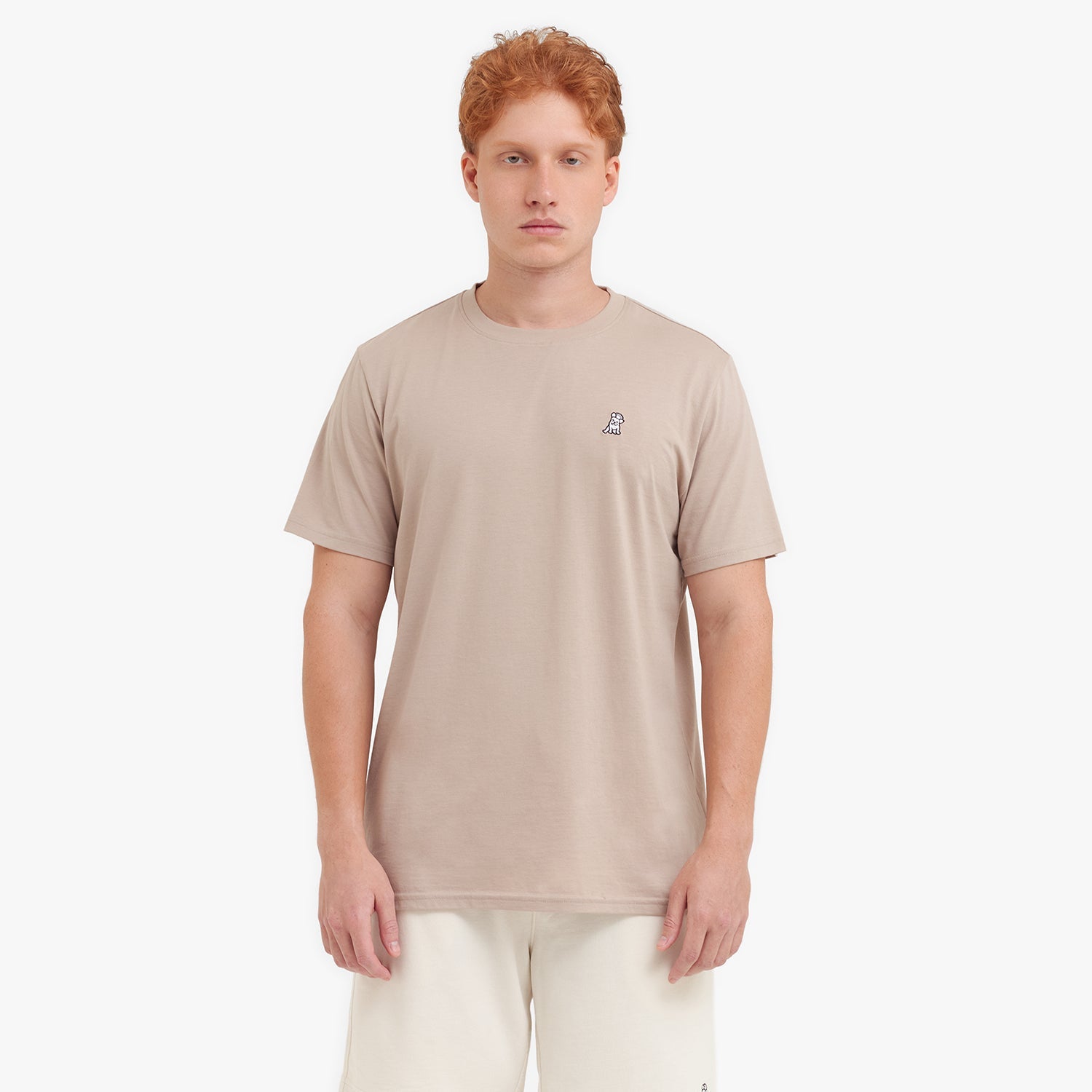 Man wearing a beige t-shirt with a small logo on a white background