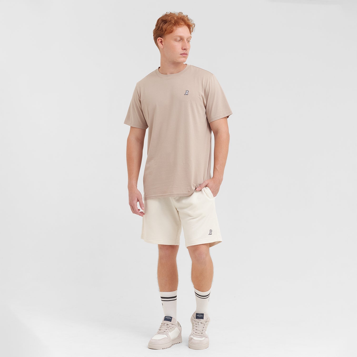 Man wearing a beige t-shirt and white shorts on a plain background