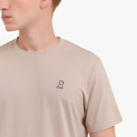 Close-up of a beige t-shirt with a small logo on the chest against a white background