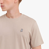 Close-up of a beige t-shirt with a small logo on the chest against a white background