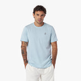 Man wearing a light blue t-shirt with a small logo on a white background