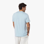 Back view of a man wearing a light blue t-shirt and white pants on a white background