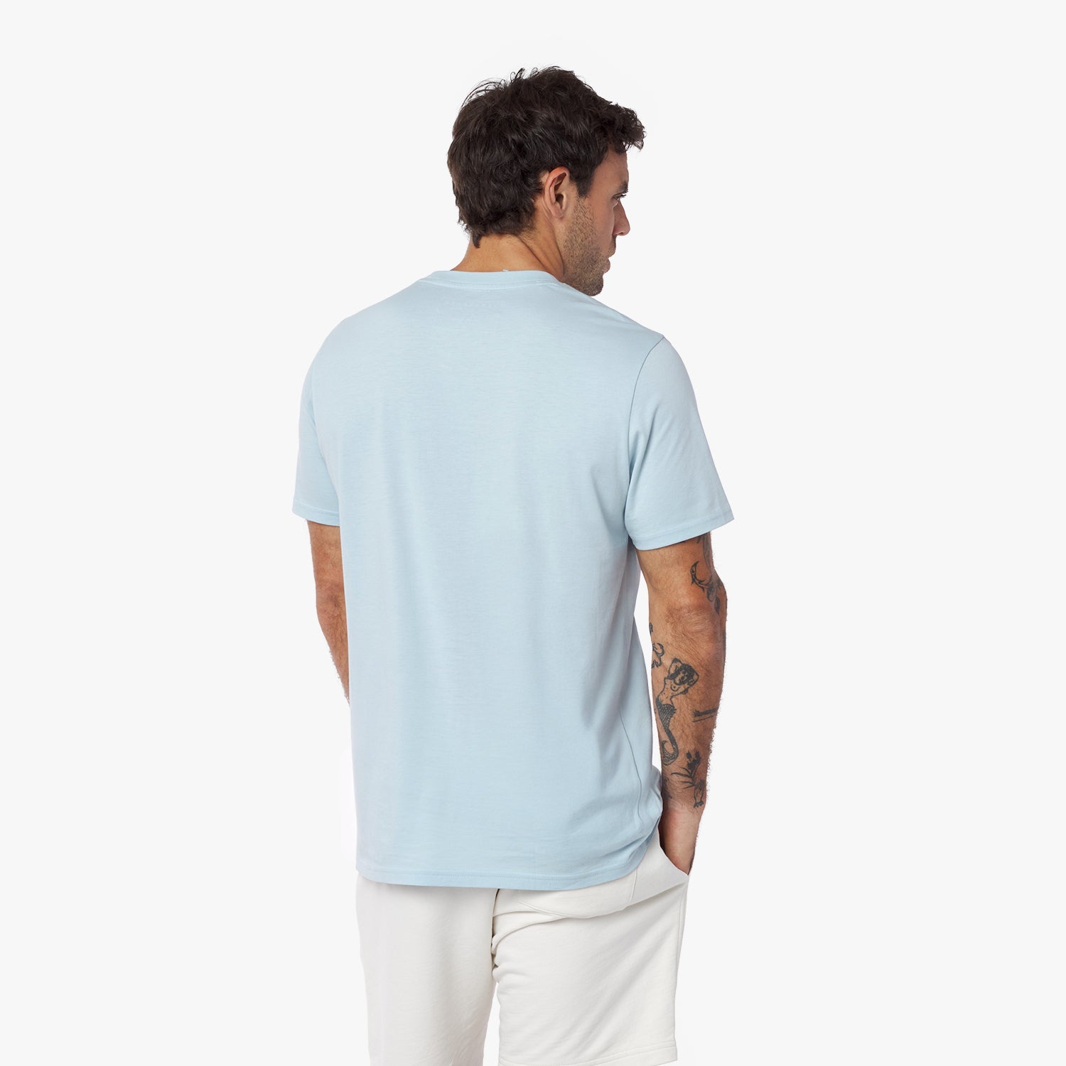 Back view of a man wearing a light blue t-shirt and white pants on a white background