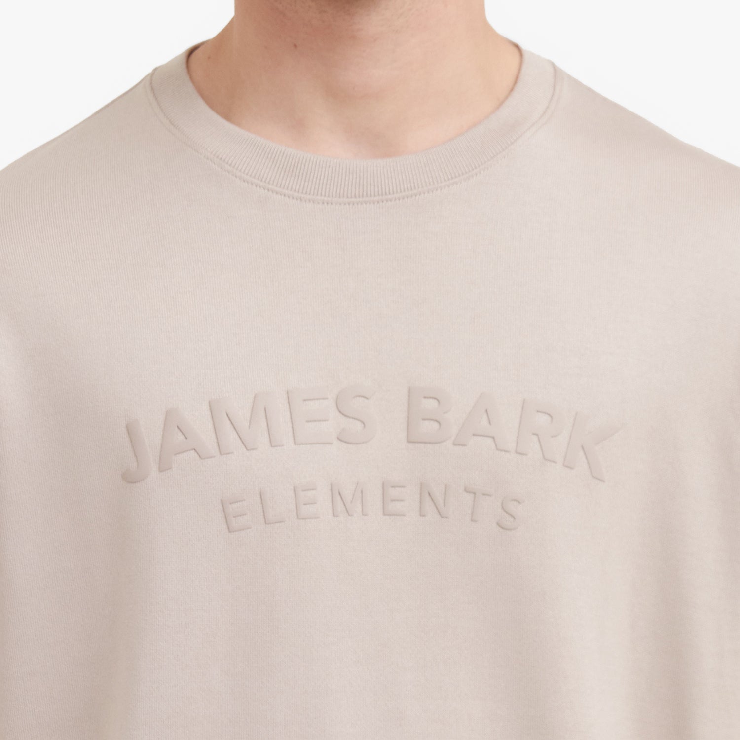 Close-up of a beige sweatshirt with 'James Bark Elements' text on a white background