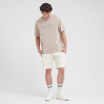 Man wearing a beige t-shirt and white shorts on a plain background
