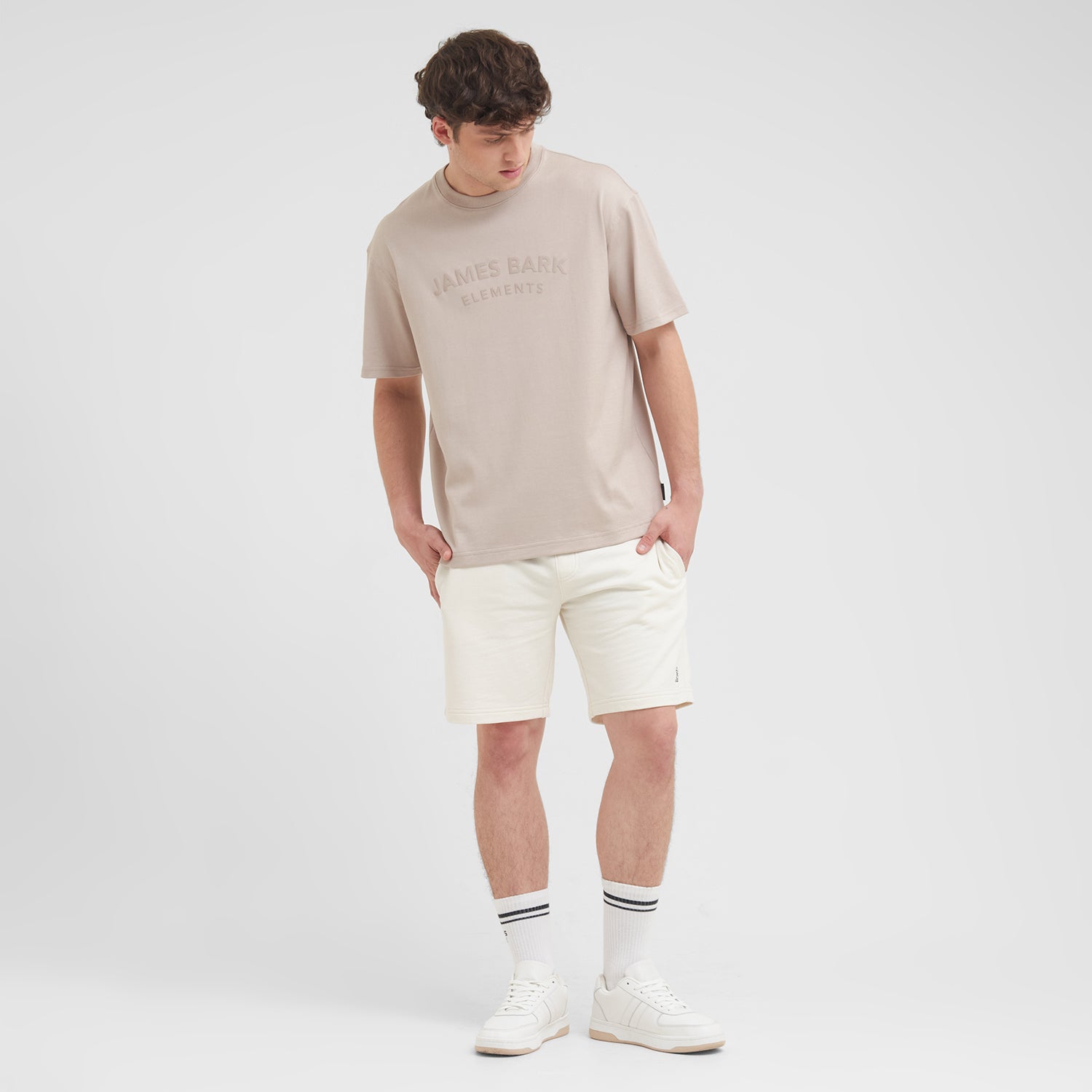 Man wearing a beige t-shirt and white shorts on a plain background