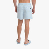 A man is shown from the back wearing light blue swim shorts and matching slide sandals
