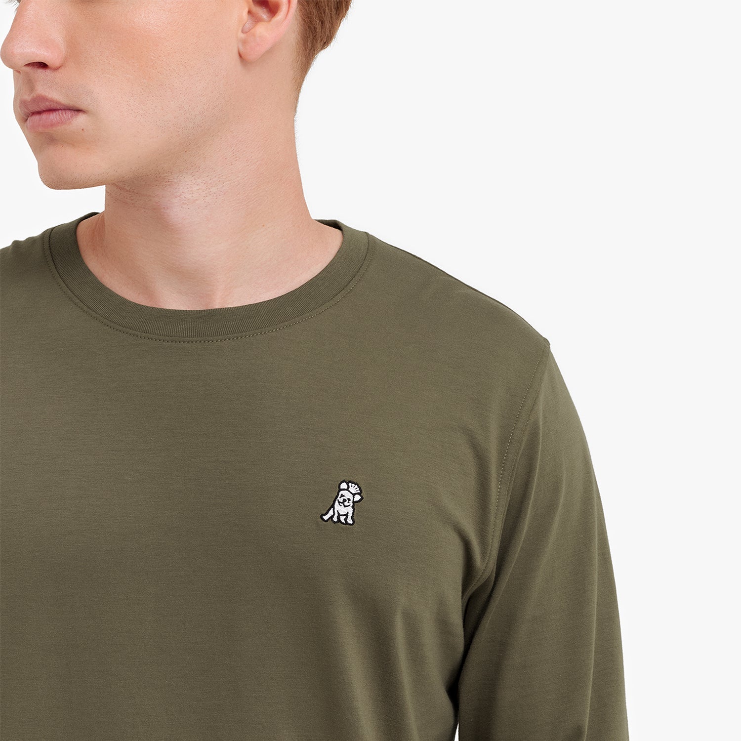 Close-up of the olive green shirt, showing the crew neck and a small embroidered logo on the chest.