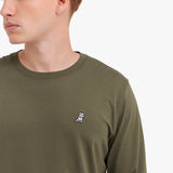 Close-up of the olive green shirt, showing the crew neck and a small embroidered logo on the chest.