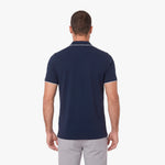 A man viewed from the back wearing a navy blue short-sleeve polo shirt with thin white piping trim on the collar and sleeve cuffs, paired with light gray trousers, against a plain white background.